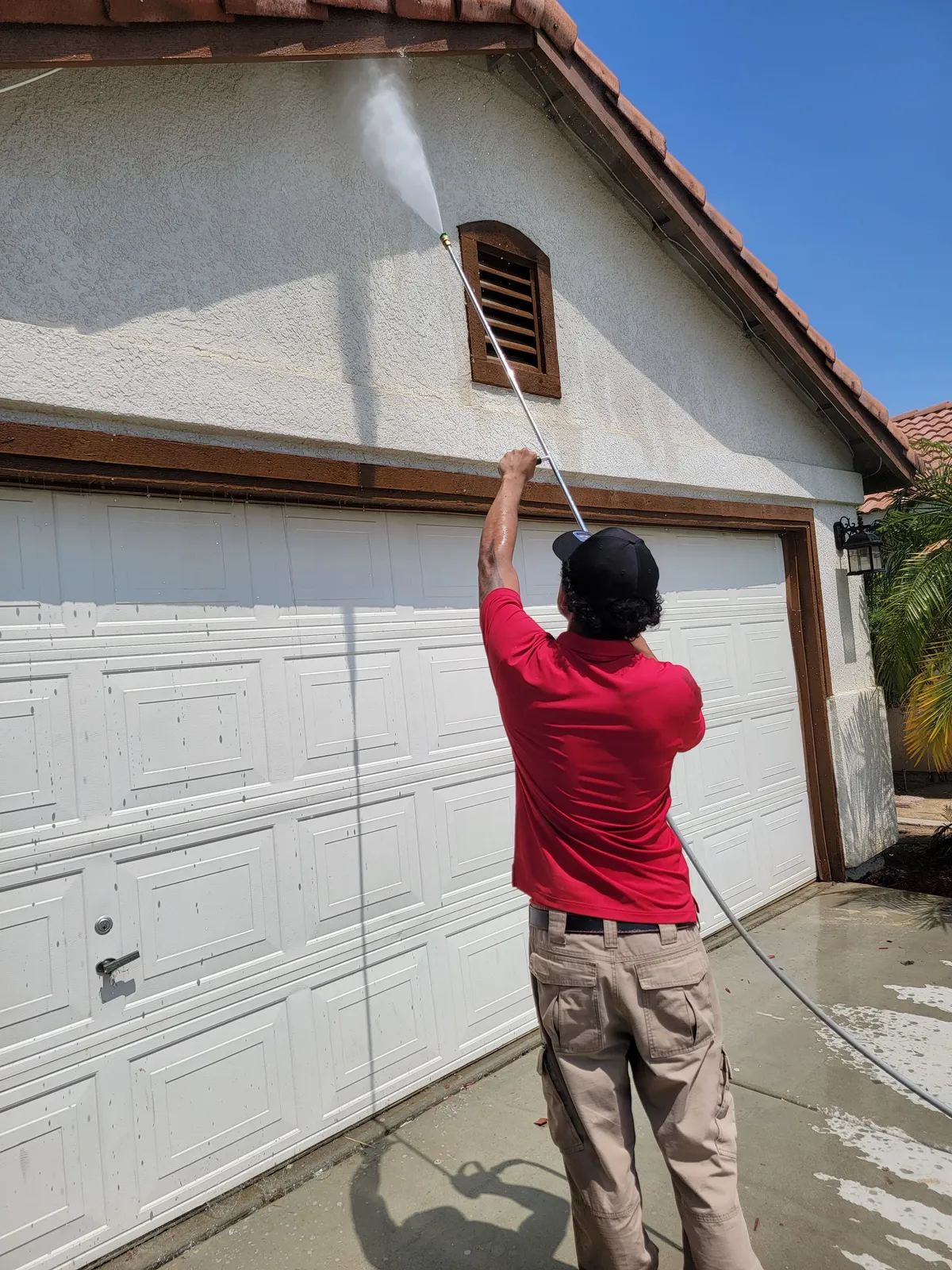 Soft wash house washing in Bakersfield, CA — low-pressure cleaning of upper stucco, eaves, and trim on a Bakersfield home exterior
